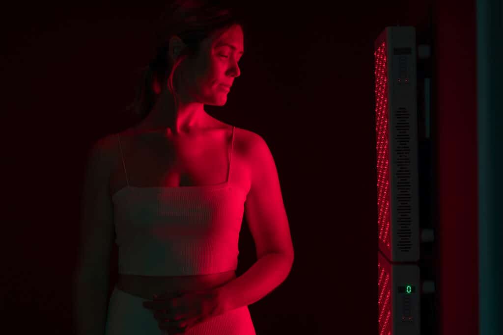 Mature woman receiving red light therapy. Woman standing next to a red light device in a beauty spa. Anti-aging and skin care treatment.